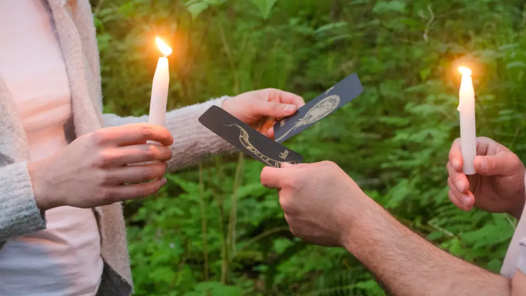 Due persone giocano alla foresta notturna, candele accese e carte esposte, ma illeggibili.